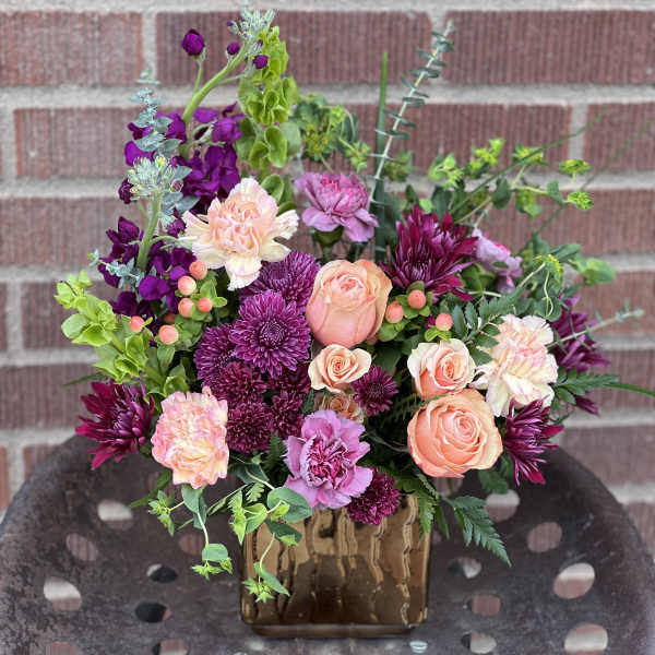 Mixed bouquet of peach, pink, and purple flowers in a brown vase