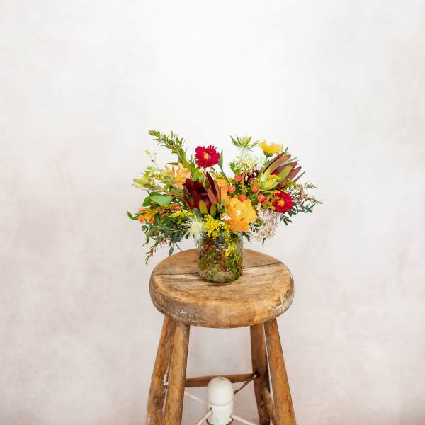 Mixed bouquet in a glass jar on a wooden stool