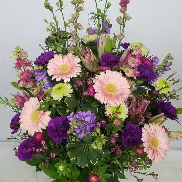 Mixed pink, purple, and green floral arrangement in a brown urn