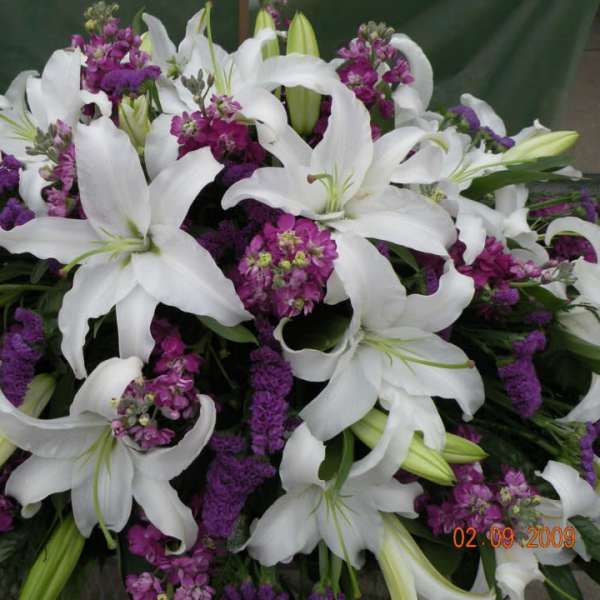 White lilies and purple flowers in a dense arrangement
