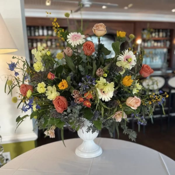 Mixed floral arrangement in a white pedestal vase with roses and daisies