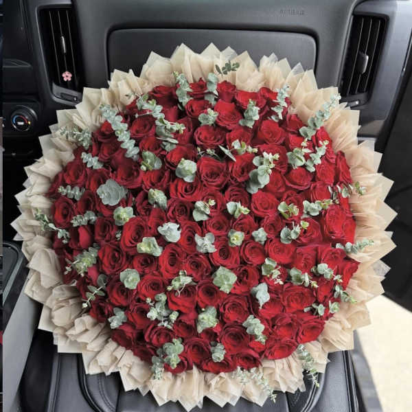 Large bouquet of red roses wrapped in beige paper with eucalyptus accents