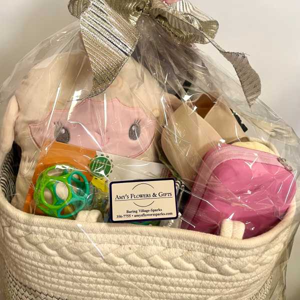 Gift basket with a plush doll, toy ball, and pink pouch wrapped in cellophane