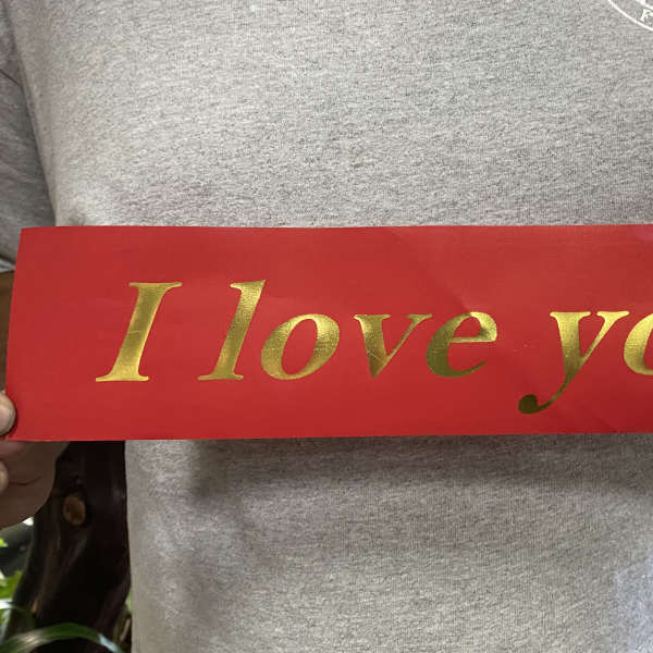 Person holding a red sign that says "I love you" in gold letters