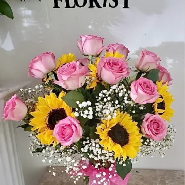 Pink roses and sunflowers arranged in a glass vase with baby's breath