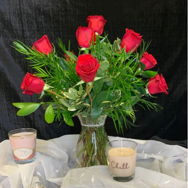 Red roses in a clear glass vase with candles on white fabric
