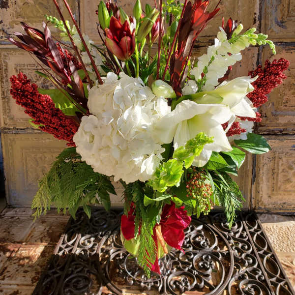 Tall floral arrangement with white hydrangeas, lilies, and red accents in a vase