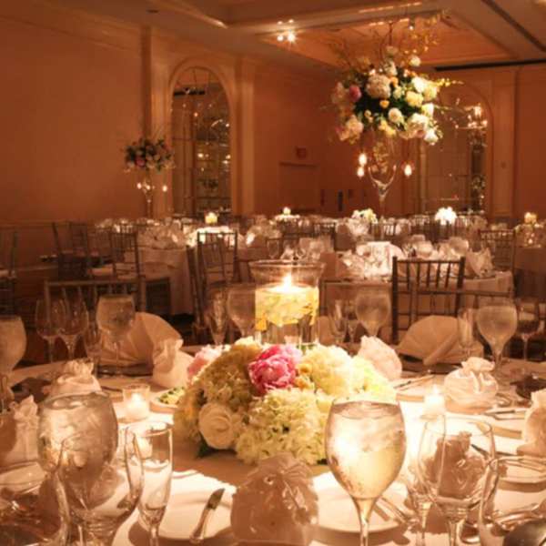 Floral centerpieces on round banquet tables in a warmly lit ballroom