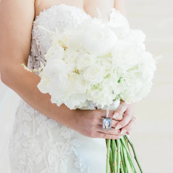 Bride holding a white wedding bouquet with a photo charm