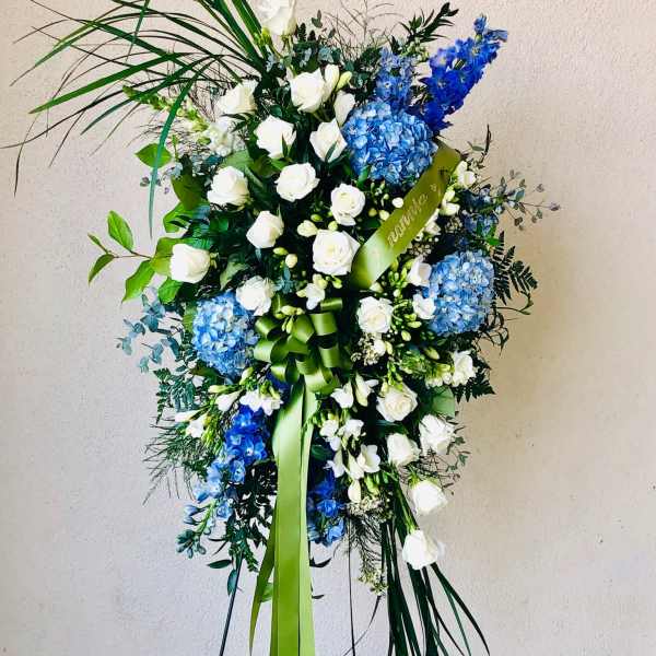Standing floral spray with white roses and blue hydrangeas on a ribboned easel
