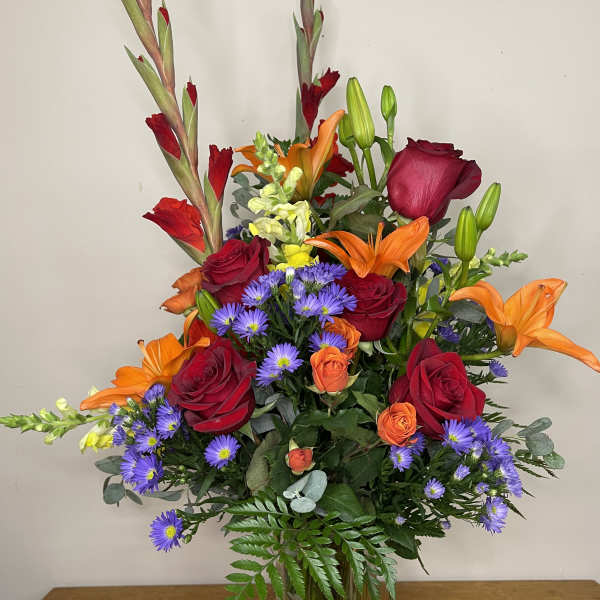 Mixed bouquet of red roses, orange lilies, and purple daisies in a clear vase