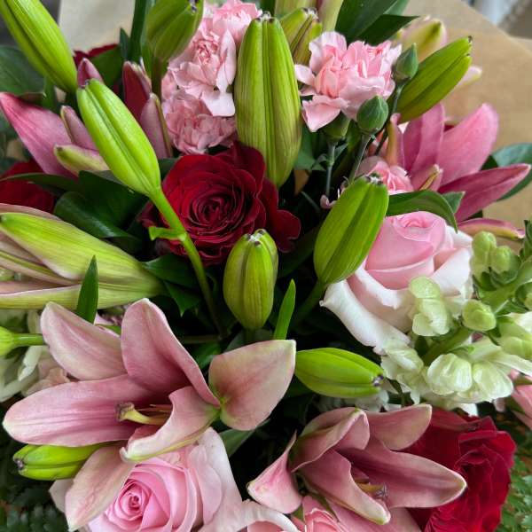 Bouquet of pink lilies, roses, and carnations with a red rose accent