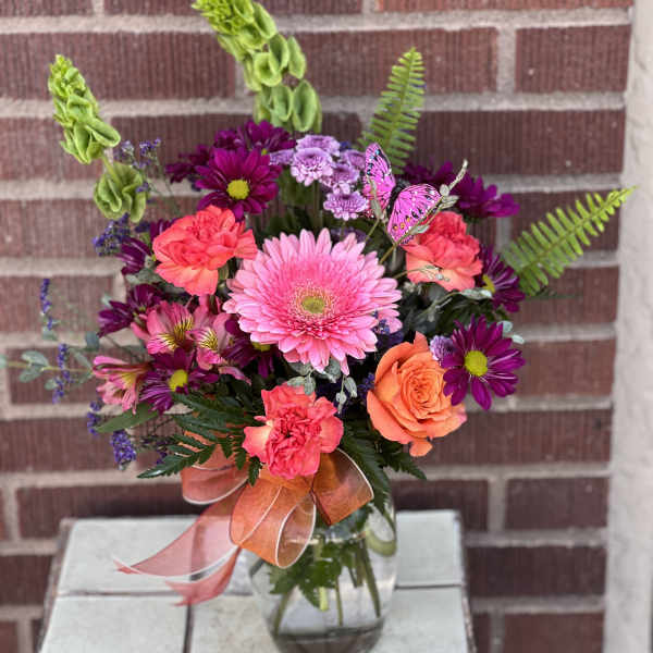 Mixed pink, purple, and orange flowers in a glass vase with a ribbon