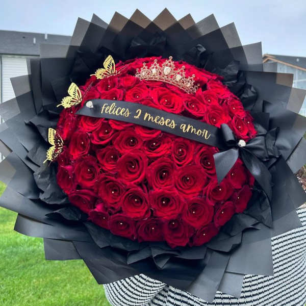 Large bouquet of red roses wrapped in black paper with a crown and ribbon