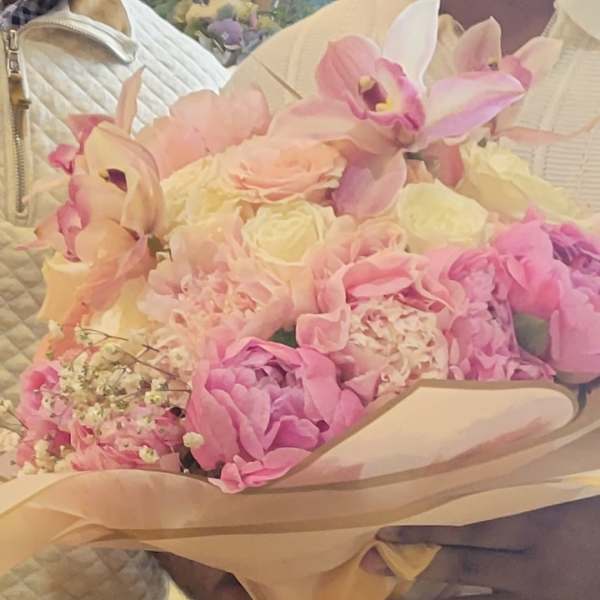 Pink and cream bouquet with orchids, roses, and hydrangeas wrapped in beige paper