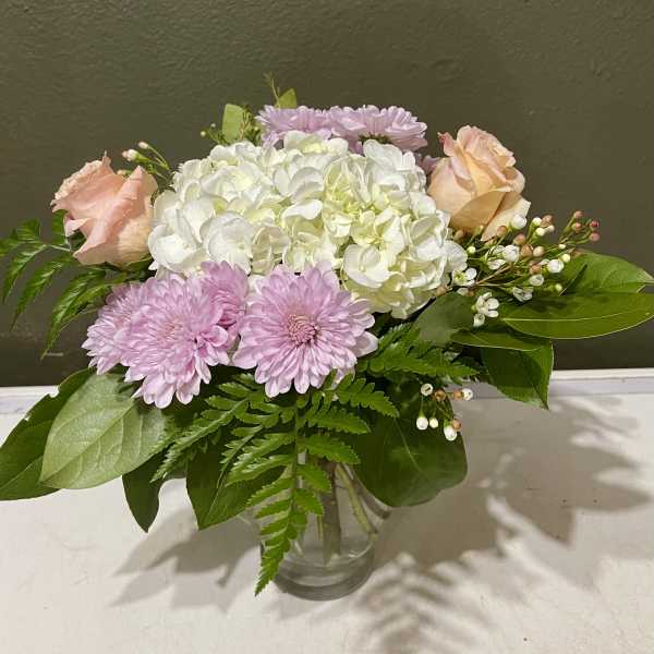 Pink roses and chrysanthemums arranged with white hydrangea in a glass vase.
