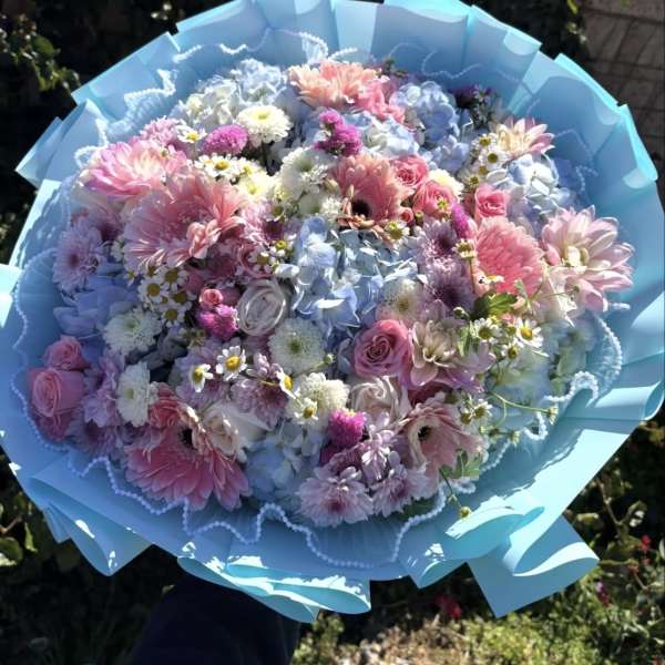 Large pastel bouquet of pink, blue, and white flowers wrapped in blue paper