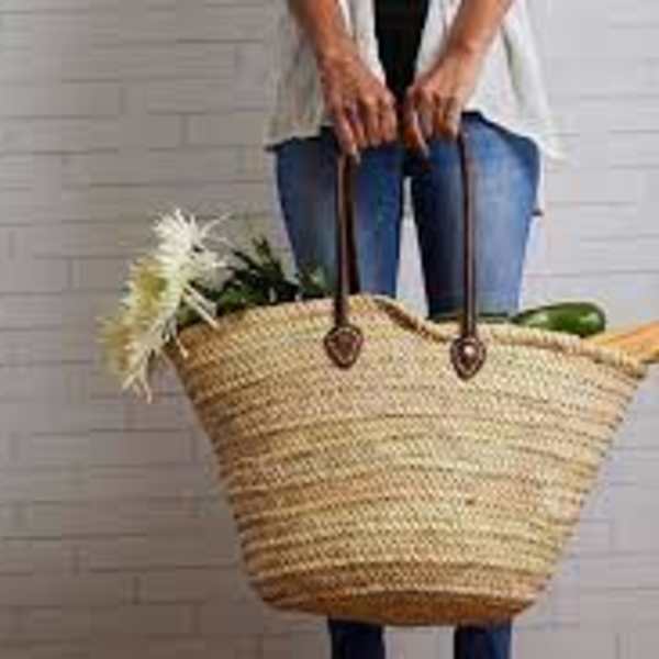 Person holding a large woven market basket with groceries and flowers