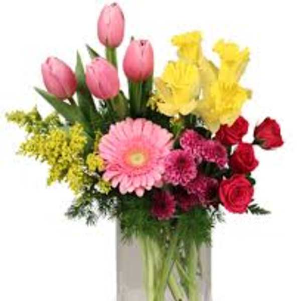 Mixed bouquet of pink tulips, yellow lilies, red roses, and pink gerbera daisies in a glass vase
