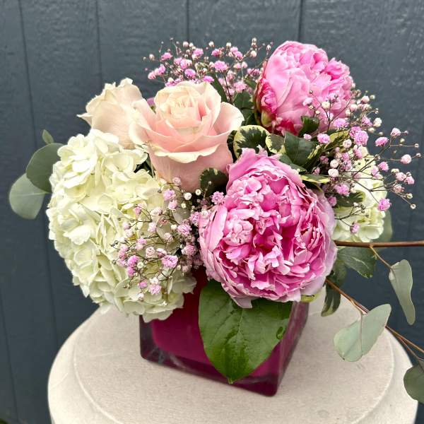 Pink roses and peonies arranged with white hydrangeas in a magenta vase