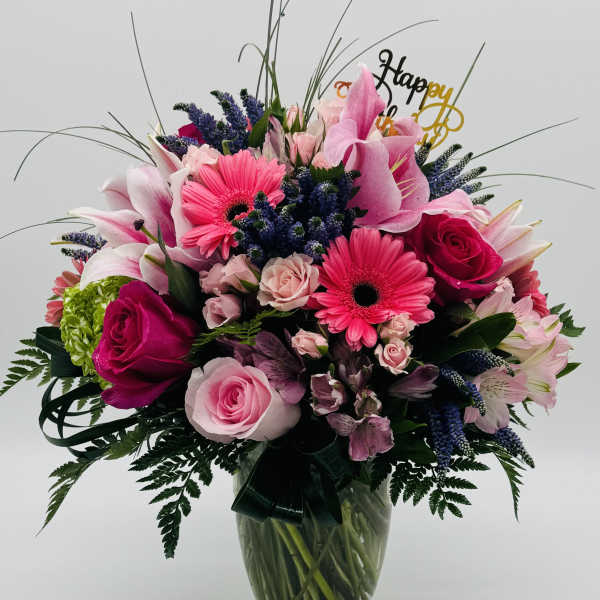 Mixed pink and purple bouquet in a glass vase with a Happy Birthday topper