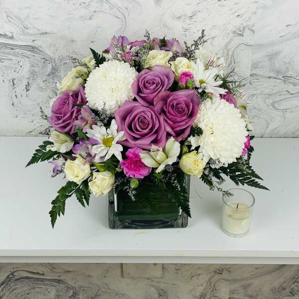 Pink and white rose bouquet in a square glass vase with a small candle beside it.