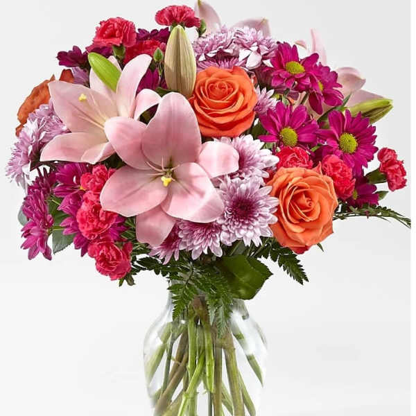 Mixed bouquet of pink lilies, roses, and purple daisies in a glass vase