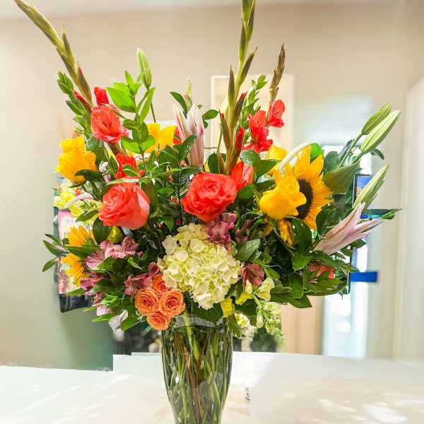 Bright mixed bouquet in a glass vase with sunflowers, roses, and lilies