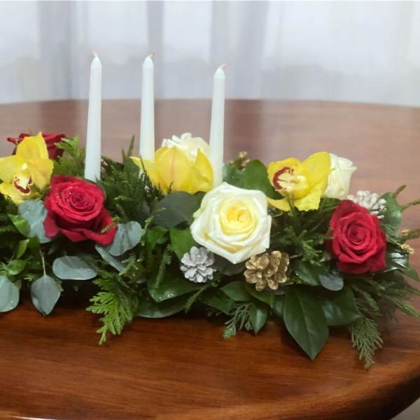 Low floral centerpiece with roses, orchids, and three white candles