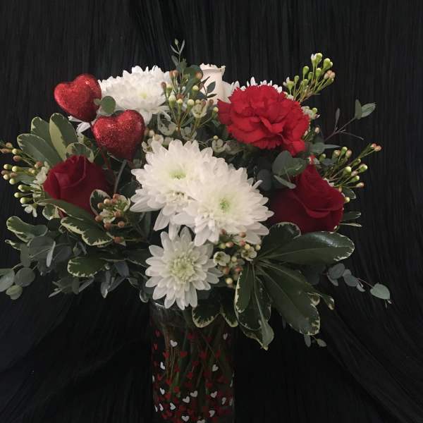 Bouquet of red and white flowers in a heart-decorated glass vase