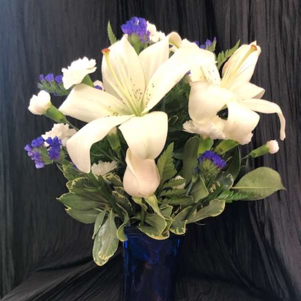 White lilies and purple filler flowers in a blue glass vase