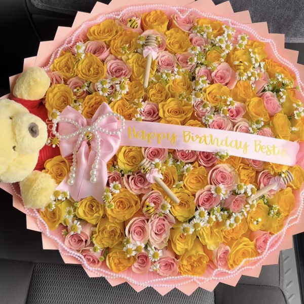 Round bouquet of pink and yellow roses with a teddy bear and birthday ribbon