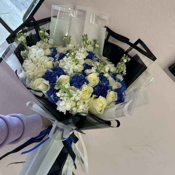 Bouquet of white roses and blue hydrangeas wrapped in black and clear paper