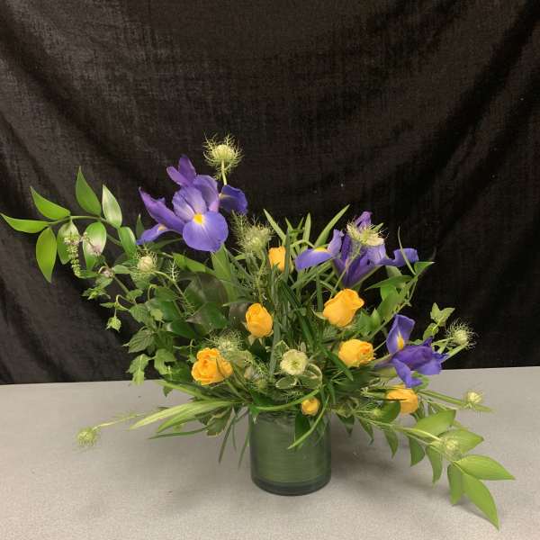 Purple iris and yellow roses arranged in a glass vase