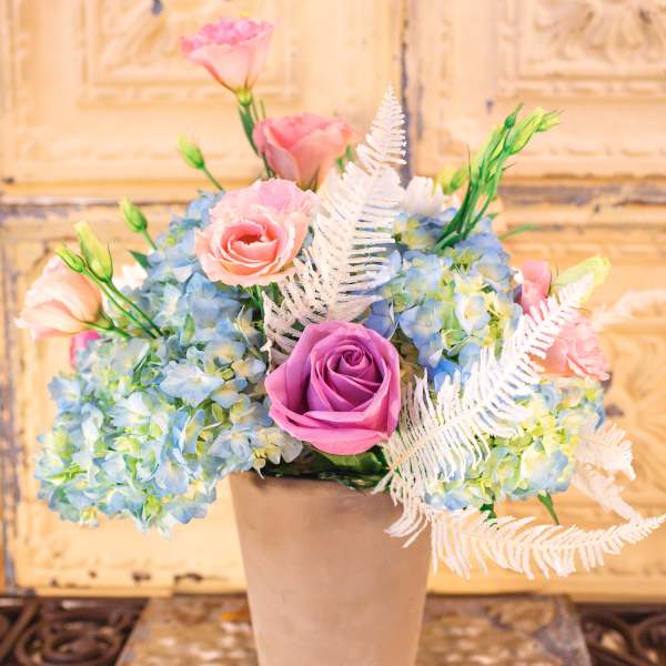 Pink and purple roses with blue hydrangeas in a beige vase