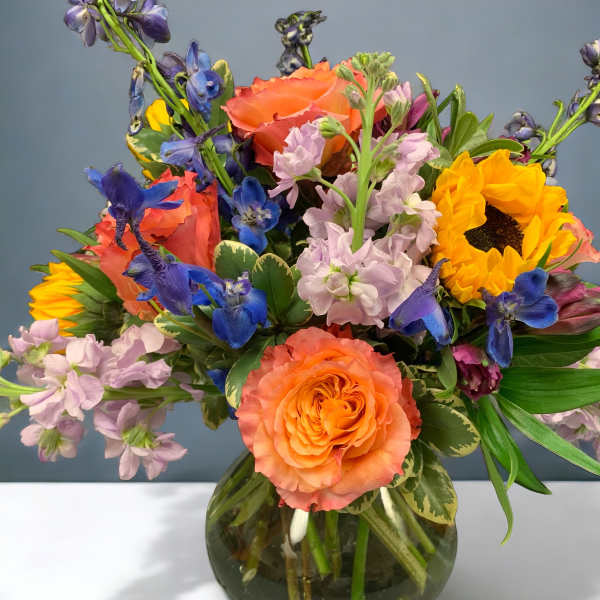 Colorful bouquet of roses, sunflowers, and blue flowers in a glass vase
