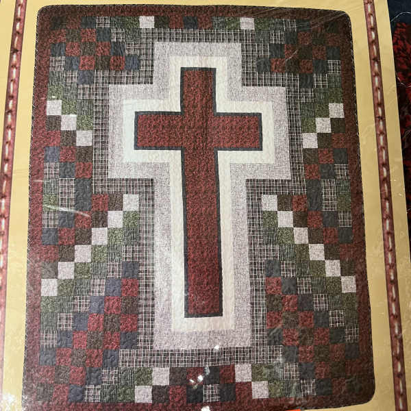 Framed quilt with a large cross pattern in red, white, and dark tones