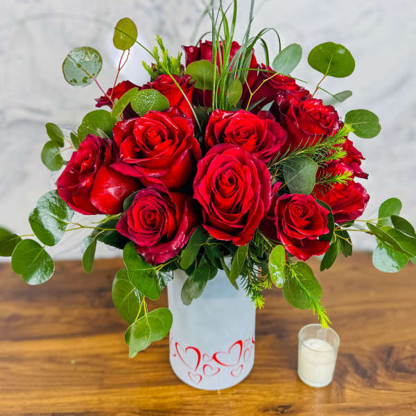 Red roses arranged in a white vase with greenery