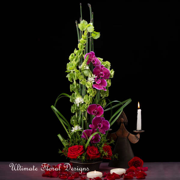 Tall floral arrangement with purple orchids, red roses, and candles