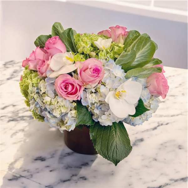 Pink roses and hydrangeas arranged in a dark vase with white orchids