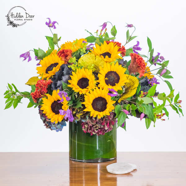 Sunflower arrangement in a glass vase with purple accent flowers