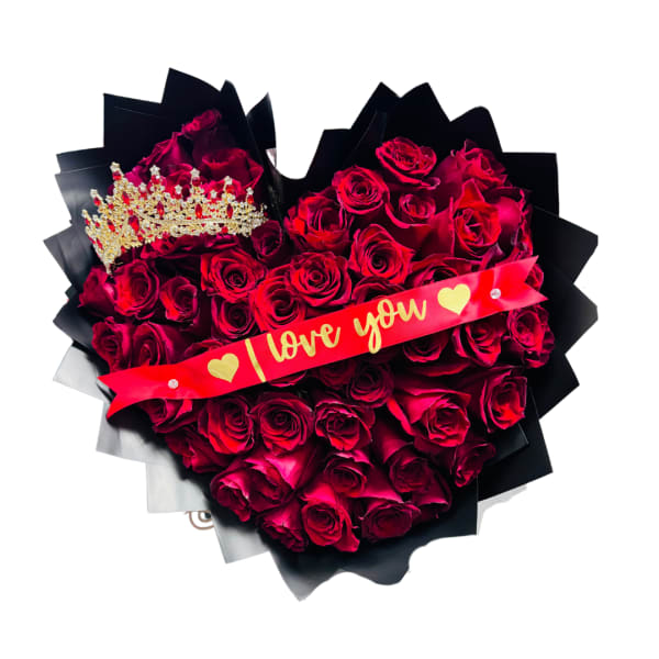 Heart-shaped arrangement of red roses with a gold crown and red love you ribbon on black wrapping.