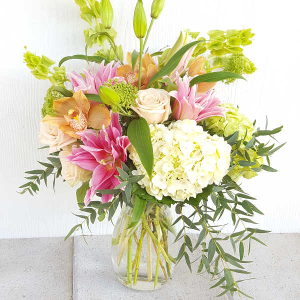 Mixed bouquet of pink lilies, cream roses, and white hydrangea in a glass vase