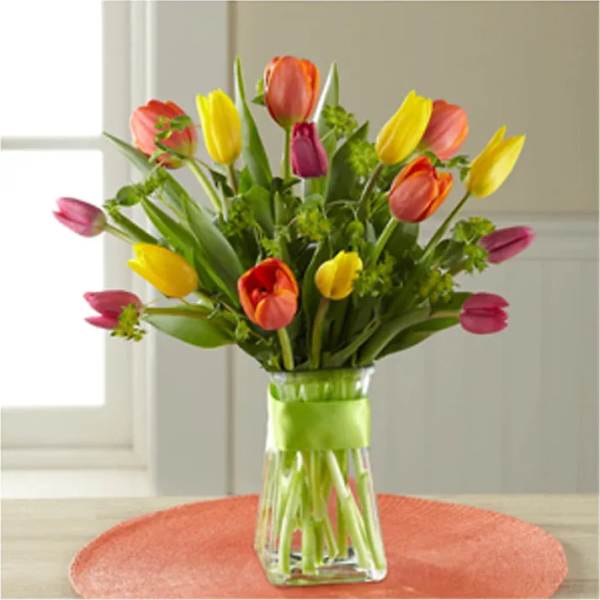 Colorful tulips arranged in a clear glass vase with a green ribbon