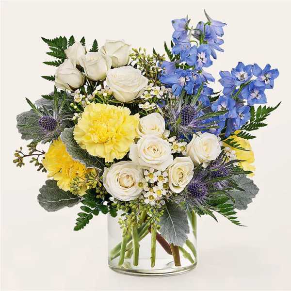 Bouquet of white roses, yellow carnations, and blue flowers in a glass vase