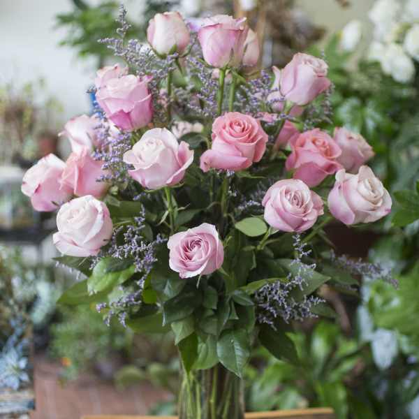 Pink roses arranged in a clear glass vase with purple filler flowers.