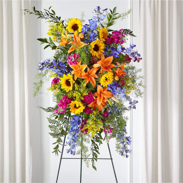 Tall standing floral spray with sunflowers, lilies, and blue flowers