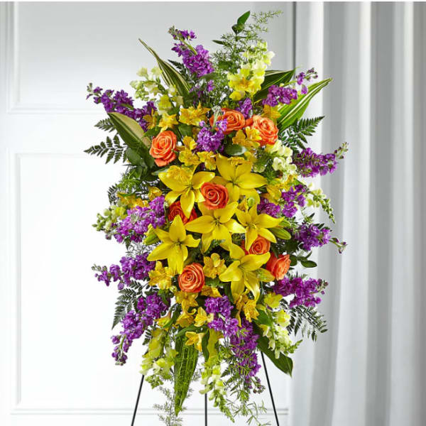 Tall standing floral spray with yellow lilies, orange roses, and purple flowers