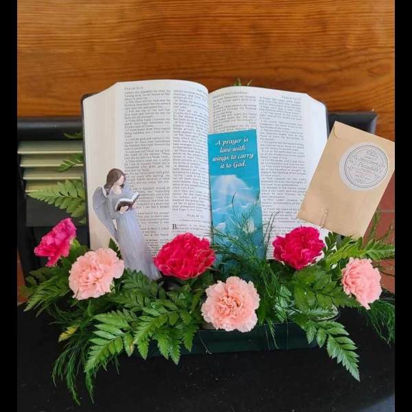 Pink carnations arranged around an open Bible with an angel figurine