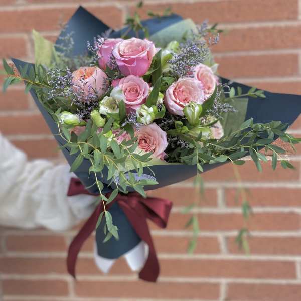 Bouquet of pink roses with purple filler and greenery wrapped in dark paper